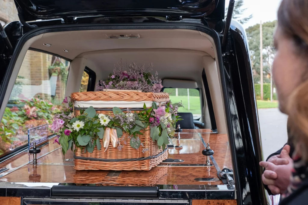 Cercueil en osier tressé fleuri à l'arrière d'un corbillard.