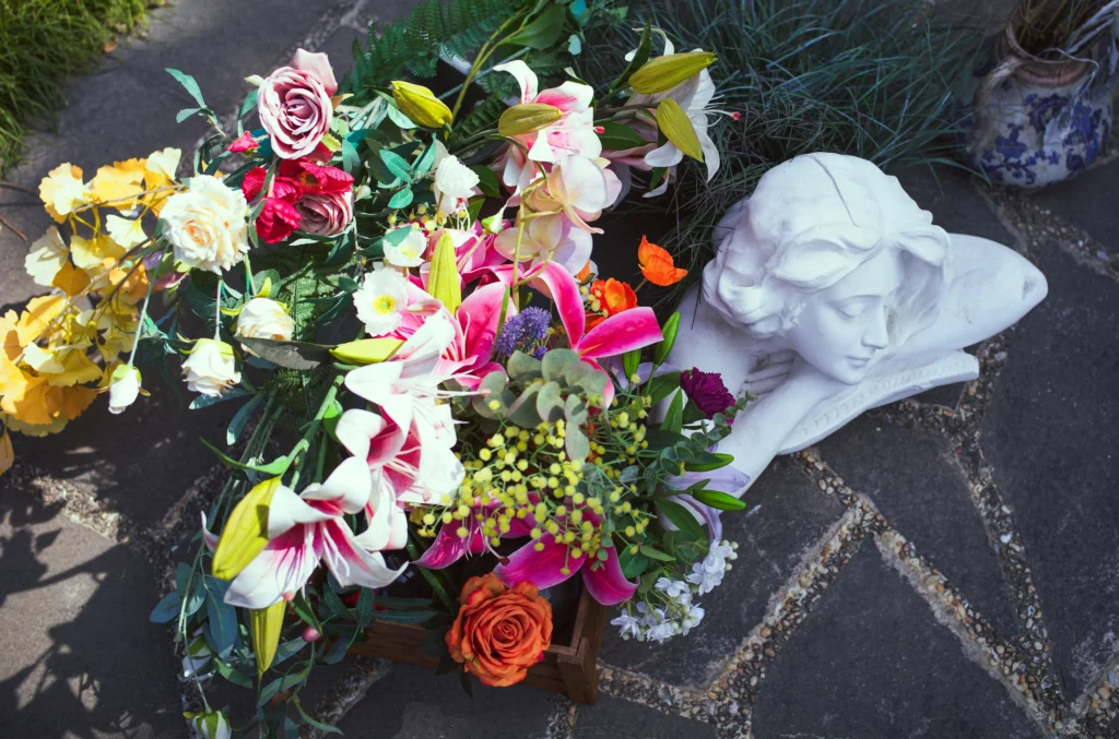 Arrangement floral de lys et roses à côté d'une statuette d'ange en marbre blanc.