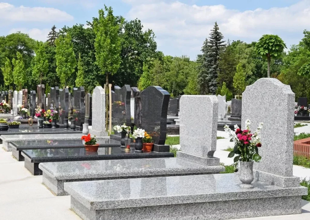 Ligne de tombes modernes en granit gris clair et foncé dans un cimetière paysager.
