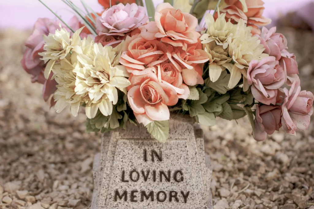 Bouquet de roses et chrysanthèmes en tissu sur une stèle 'In Loving Memory'.