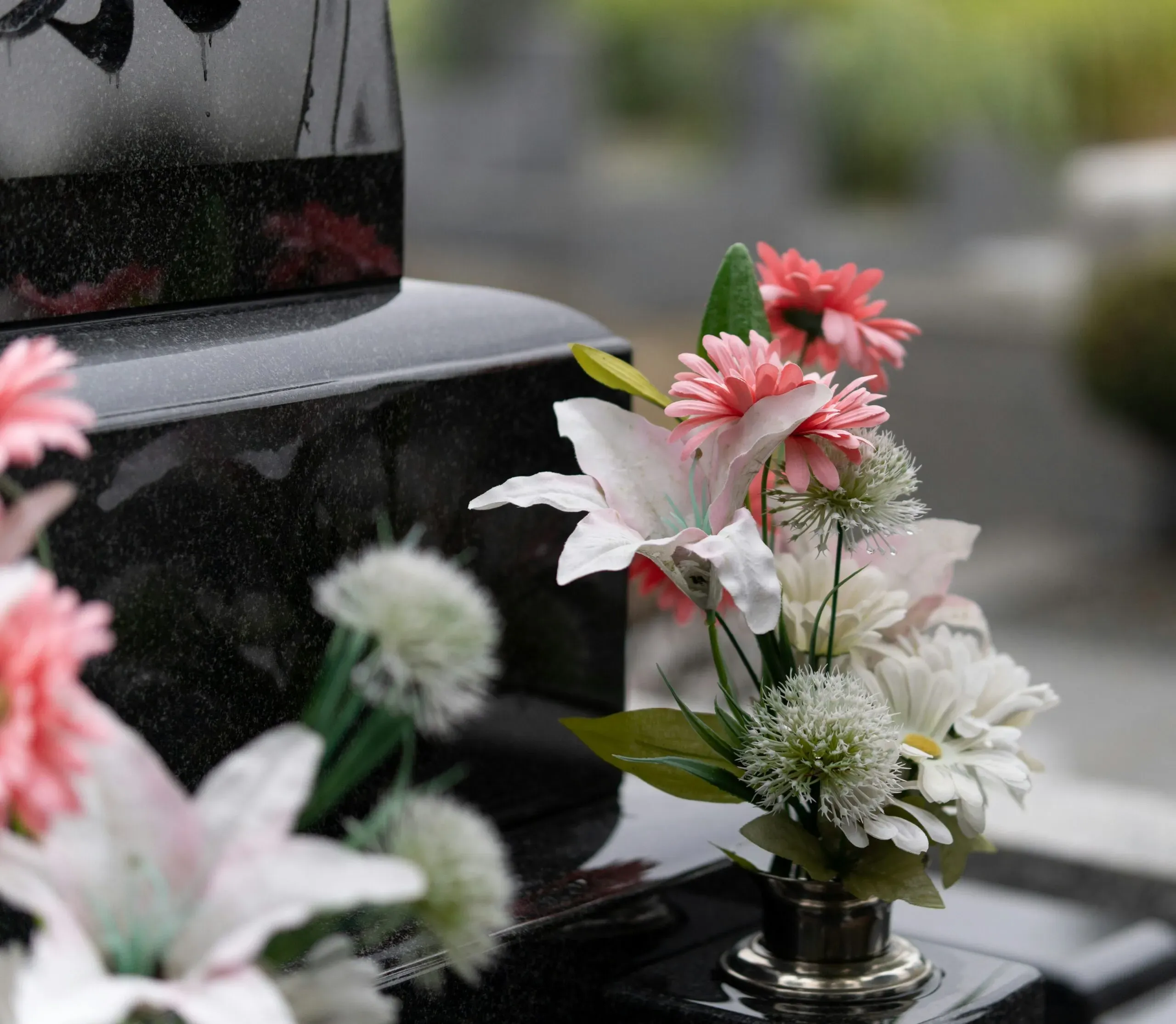 Gros plan sur un bouquet de fleurs artificielles colorées posé sur une tombe noire.